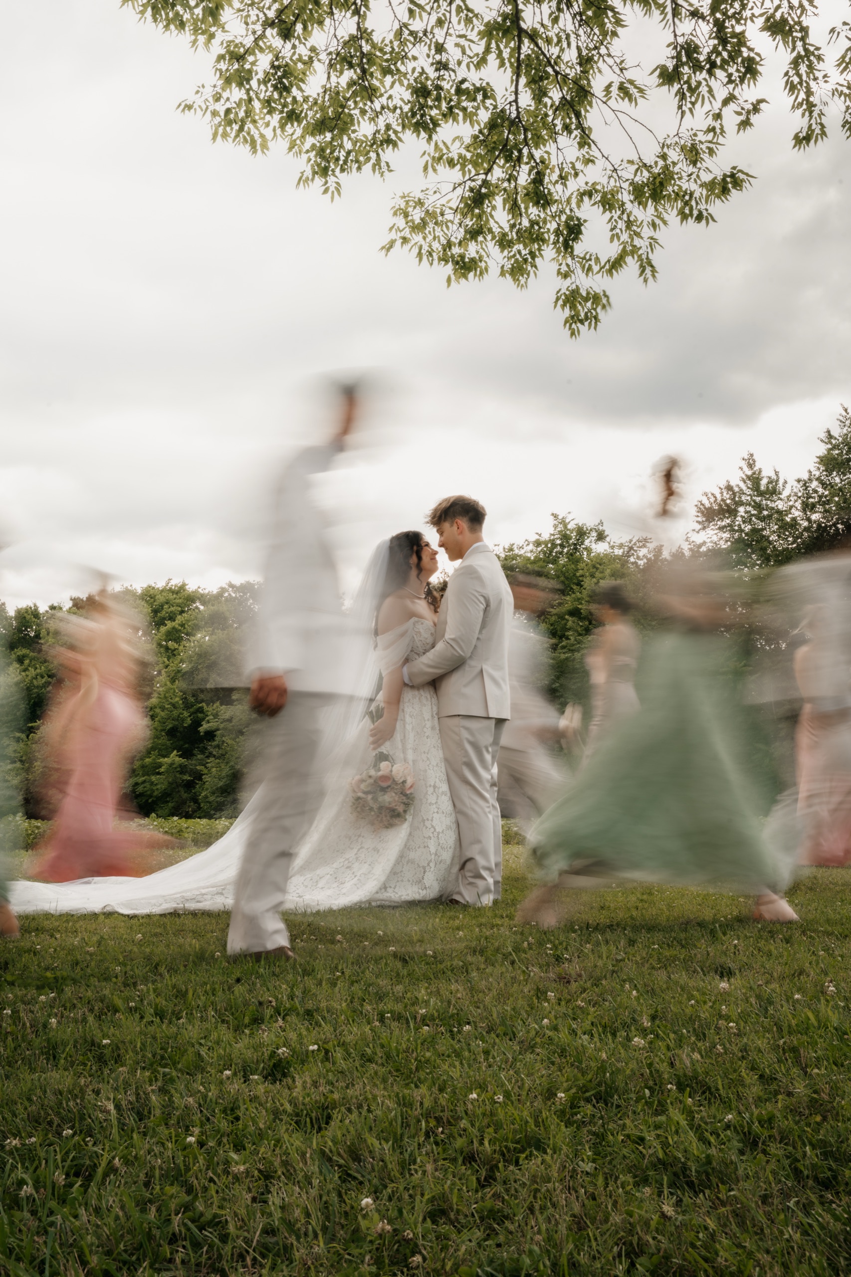 Bride and groom still at the center while their wedding party spins around them in motion blur