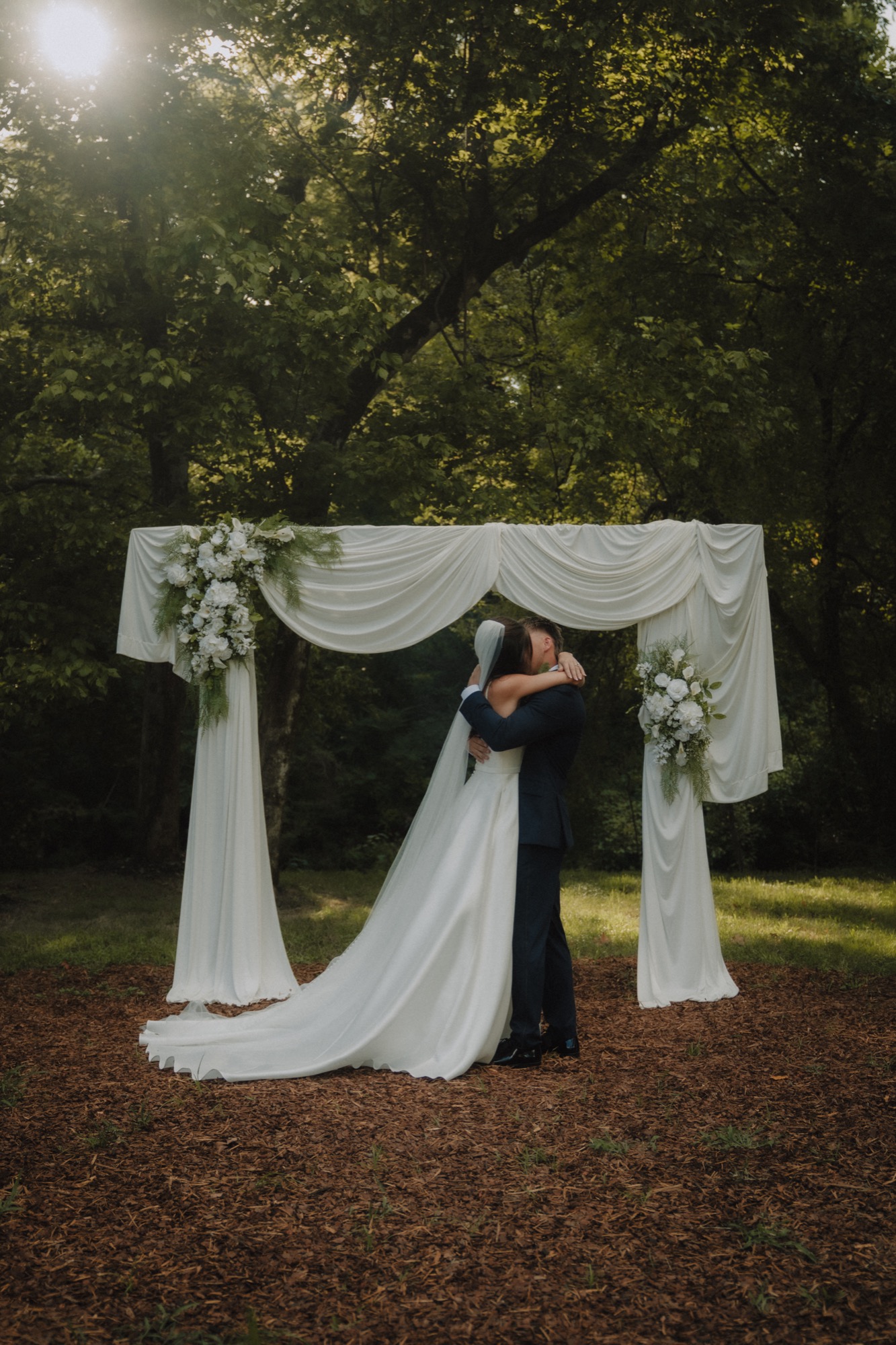 Piper and Zechariah embrace beneath the arch after the ceremony