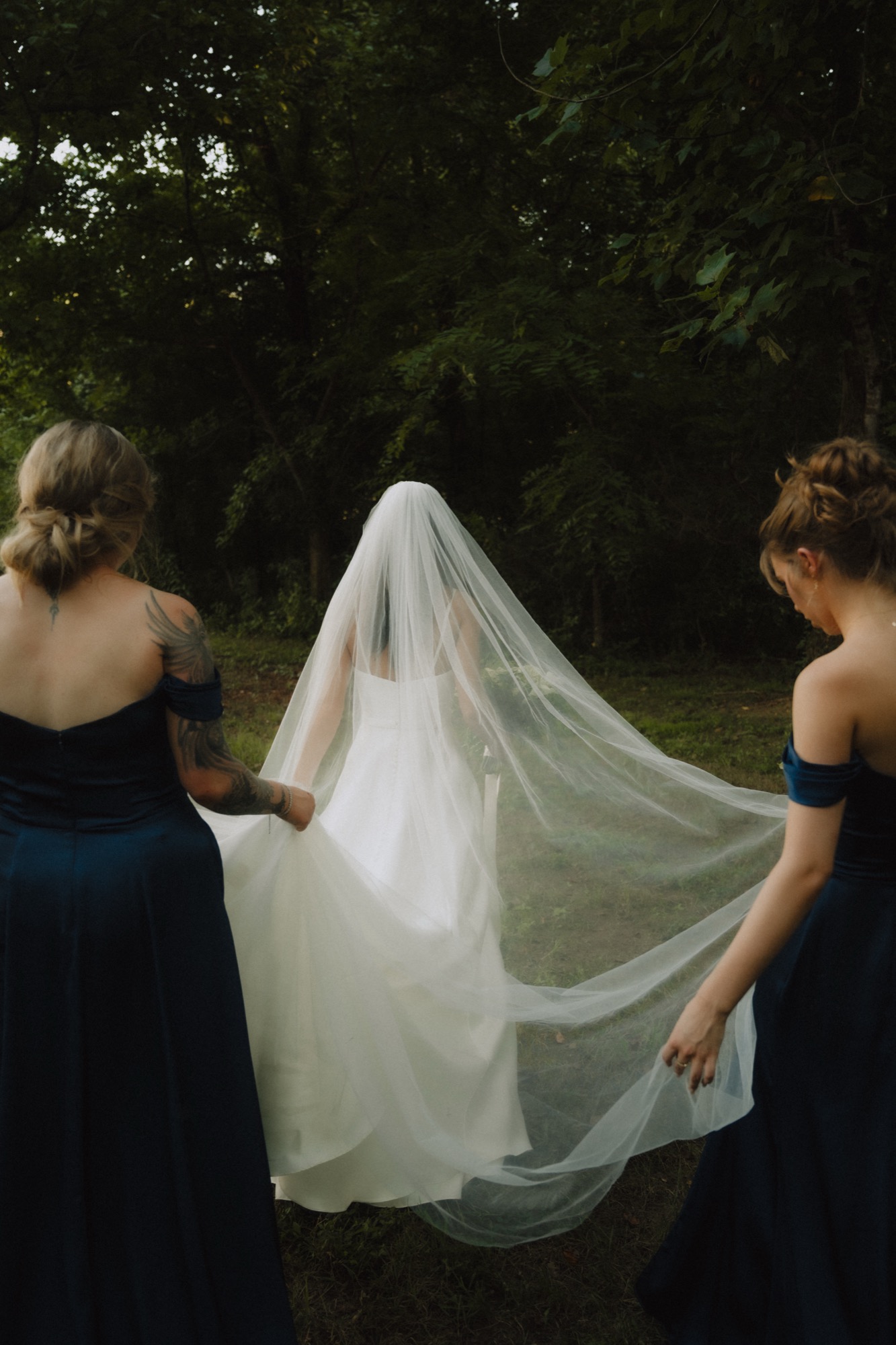 Piper's bridesmaids carrying her veil through the trees